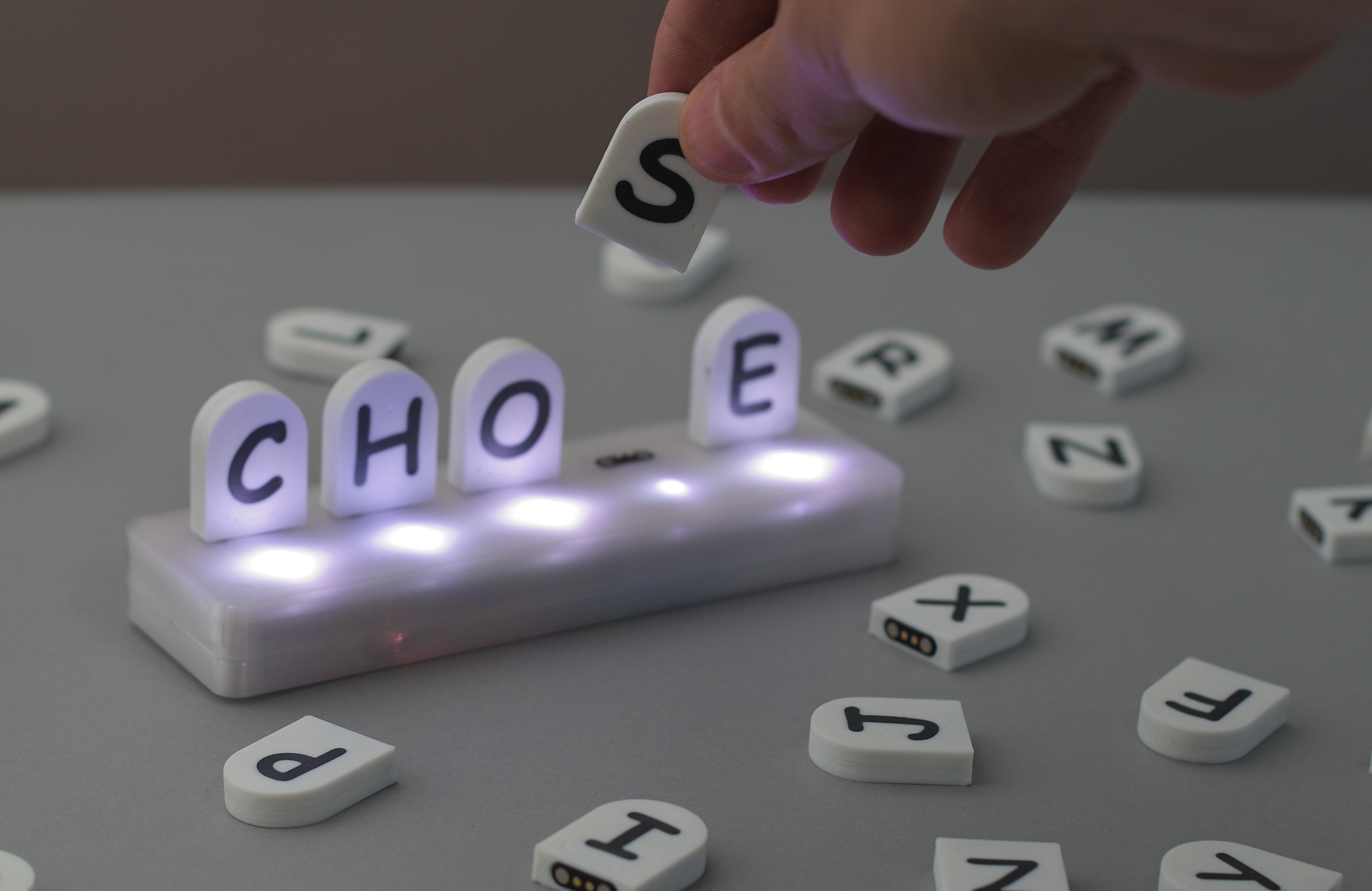 A hand lifting a magnetic letter tile from an illuminated Tactle game board